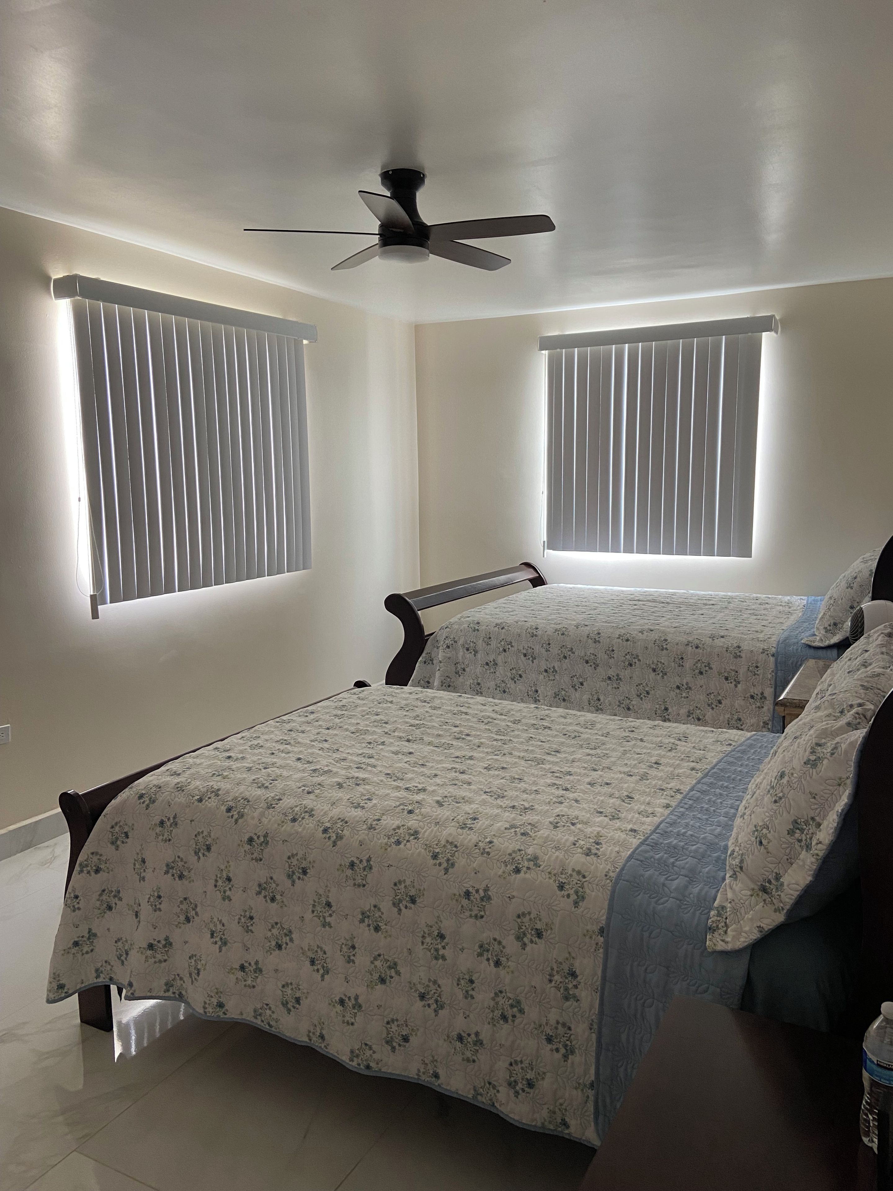 A bedroom with two beds, a ceiling fan, and windows with blinds.