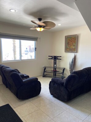 A living room with two dark sofas, a ceiling fan, a treadmill, and a window with blinds. - Casa Adriana. Comfort and safety. (El Sauzal)