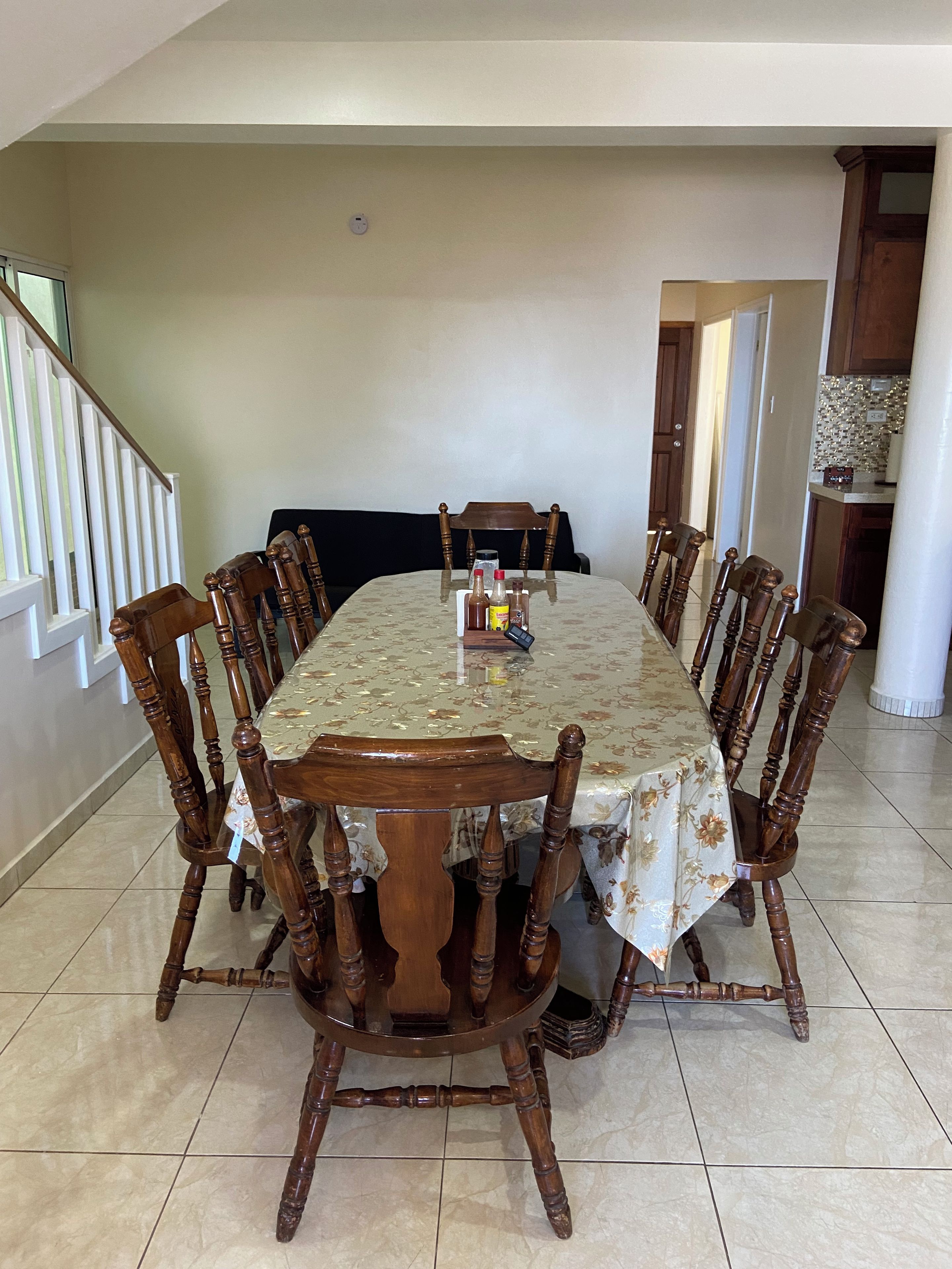 A dining room with a large table, wooden chairs, and a floral tablecloth.