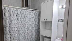 Ein Badezimmer mit gemustertem Duschvorhang, Toilette, Waschbecken und einem Schrank.