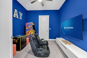 Ett rum med en blå vägg, en PlayStation TV, en spelmaskin i arkadstil och en rad svarta spelstolar.