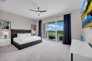 Ett modernt hotellrum med en stor säng, en takfläkt, en platt-TV, ett skrivbord och en balkong med utsikt över en golfbana.