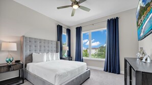A hotel room with a large bed, a nightstand with a lamp, a desk with a vase, and a view of a tropical beach through the window. - Enormous 8 Bedroom Resort Home with View of 18th Hole near Disney with Resort &. (Kissimmee)