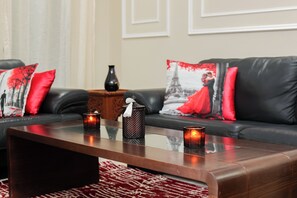 Een moderne woonkamer met een leren bank, rode en zwarte kussens, een glazen salontafel en twee kaarsen.
