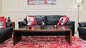 Uma sala de estar com um sofá de couro preto, uma mesa de centro de madeira e um tapete vermelho estampado.