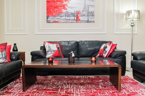 Ein Wohnzimmer mit einem schwarzen Ledersofa, einem Holztisch und einem roten Teppich mit Muster.