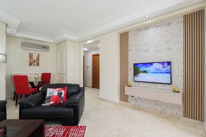 Ein modernes Wohnzimmer mit einem an einer strukturierten Wand montierten Flachbildfernseher, einem schwarzen Ledersofa mit roten Akzenten sowie einem Essbereich mit roten Stühlen.