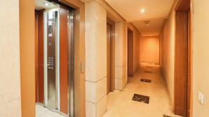 Corredor com elevador, piso ladrilhado e portas de madeira.