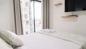 A hotel room with a bed, a TV mounted on the wall, a window with curtains, and a city view. - Newly Renovated 2BR Apartment in Lima (Lince)