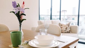 A dining table with a vase of flowers, a green mug, a white bowl, and cutlery. - Newly Renovated 2BR Apartment in Lima (Lince)