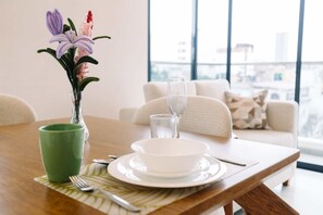 A dining table with a vase of flowers, a green mug, a white bowl, and cutlery. - Newly Renovated 2BR Apartment in Lima (Lince)