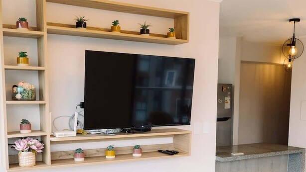 A modern living room with a flat-screen TV, a sofa, a small table, and a kitchen area in the background. - Newly Renovated 2BR Apartment in Lima (Lince)