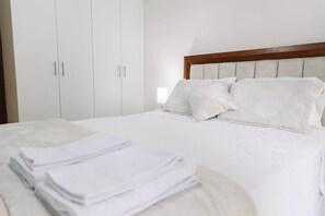 A neatly made bed with white linens and pillows, a wooden headboard, and a white wardrobe with multiple doors. - Newly Renovated 2BR Apartment in Lima (Lince)
