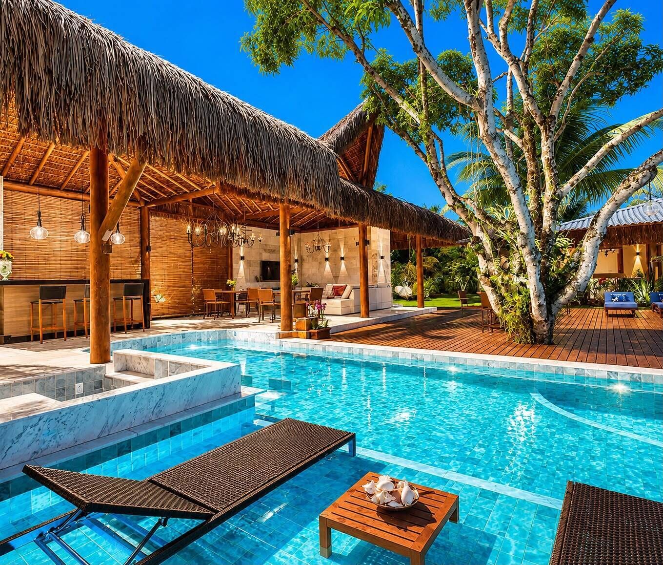 A pool area with lounge chairs, a wooden table, and a thatched-roof structure.