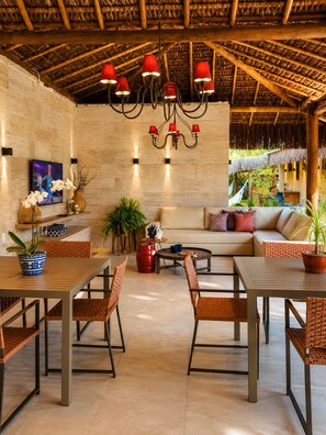 A spacious outdoor seating area with a thatched roof, a chandelier, and a variety of seating options including sofas and chairs. - Luxury Villa on the Maraú Peninsula | 4 Suites • Heated Pool • Boat & More (Maraú)