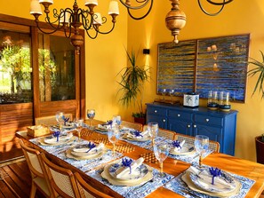 Un coin repas avec une table en bois dressée pour six personnes, des nappes bleues et blanches, et un buffet bleu orné d’objets décoratifs.