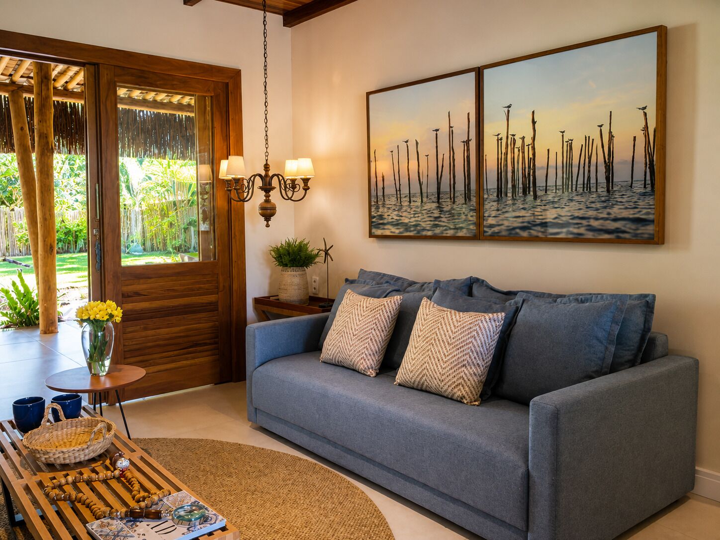 A living room with a sofa, a painting, a chandelier, and a view of the outdoors.