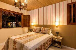 A bedroom with a bed, nightstands, a window with a view, and a chandelier.