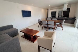 A modern living room with a sofa, a coffee table, and a dining area with chairs and a table. - Luxury & Cozy Apartment near Expo GDL / Pool & Gym (Zapopan)