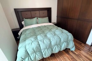A bed with a tufted headboard, a light green bedspread, and a wooden floor. - Luxury & Cozy Apartment near Expo GDL / Pool & Gym (Zapopan)