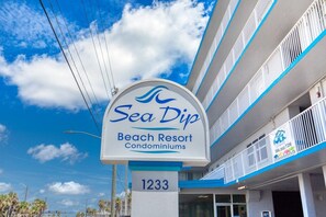 Une enseigne indiquant l’emplacement du complexe hôtelier Sea Dip Beach Resort, avec un ciel dégagé et des lignes électriques en arrière-plan.