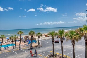 A parking lot with a pool, beach, and palm trees. - Oceanview Studio, 2 Pools, Beach, Game Room, Patio (Daytona Beach)