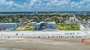 A coastal hotel with a large building, a parking lot, and a beach in the foreground. - Oceanview Studio, 2 Pools, Beach, Game Room, Patio (Daytona Beach)