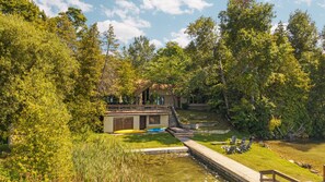A lakeside cabin with a dock, surrounded by dense trees and a small pond.