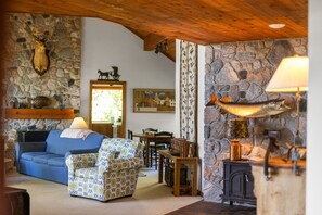 A cozy living room with a stone wall, a fireplace, a blue sofa, and a patterned armchair.