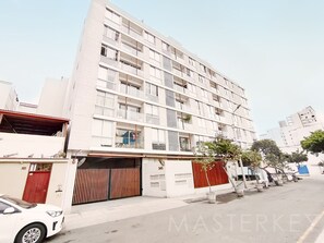A multi-story building with a flat facade, large windows, and a gated entrance. - Stylish 1BR apt in vibrant Miraflores! (Miraflores)