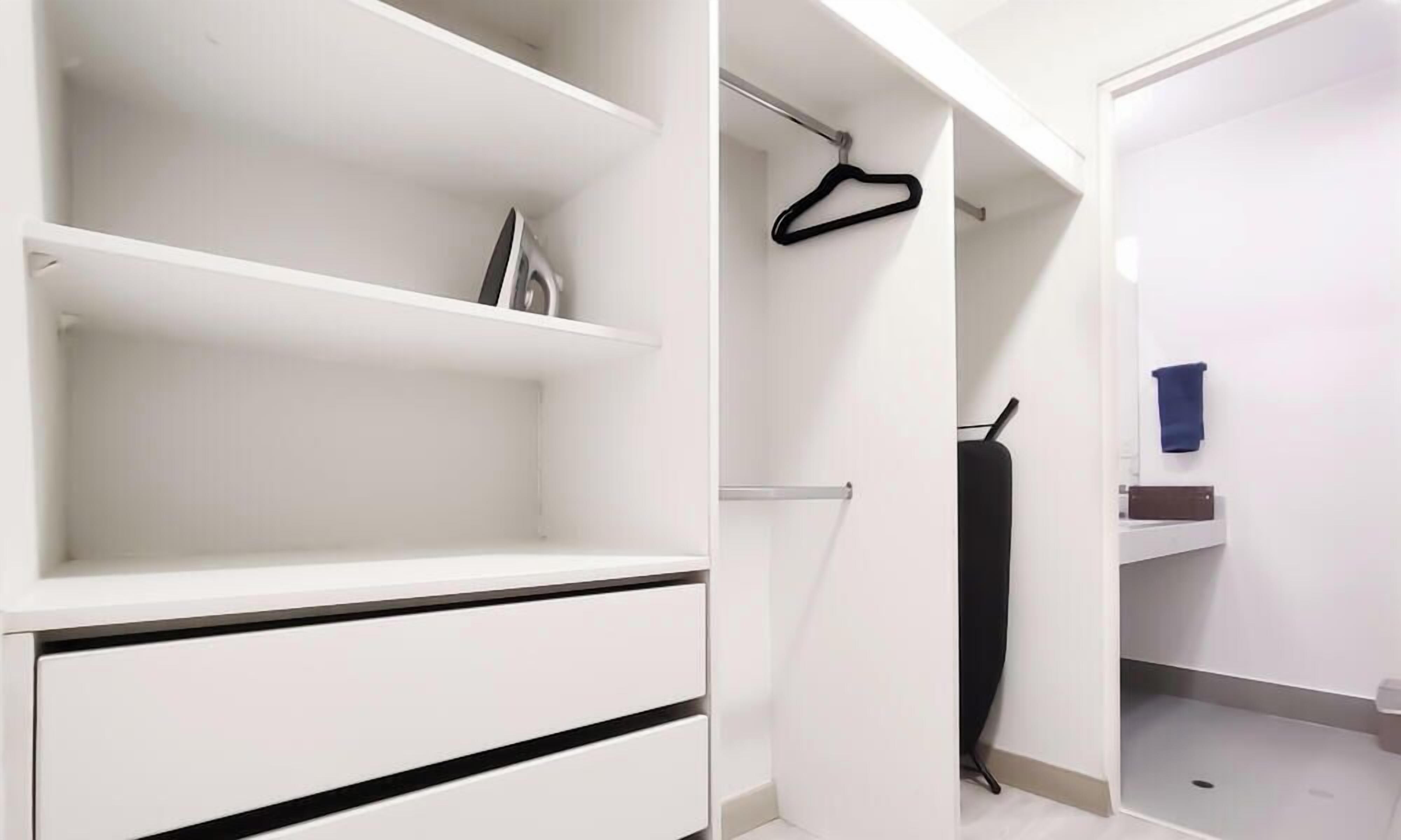 A white closet with shelves and a hanging rod, a black hanger, and a blue towel on a rack.