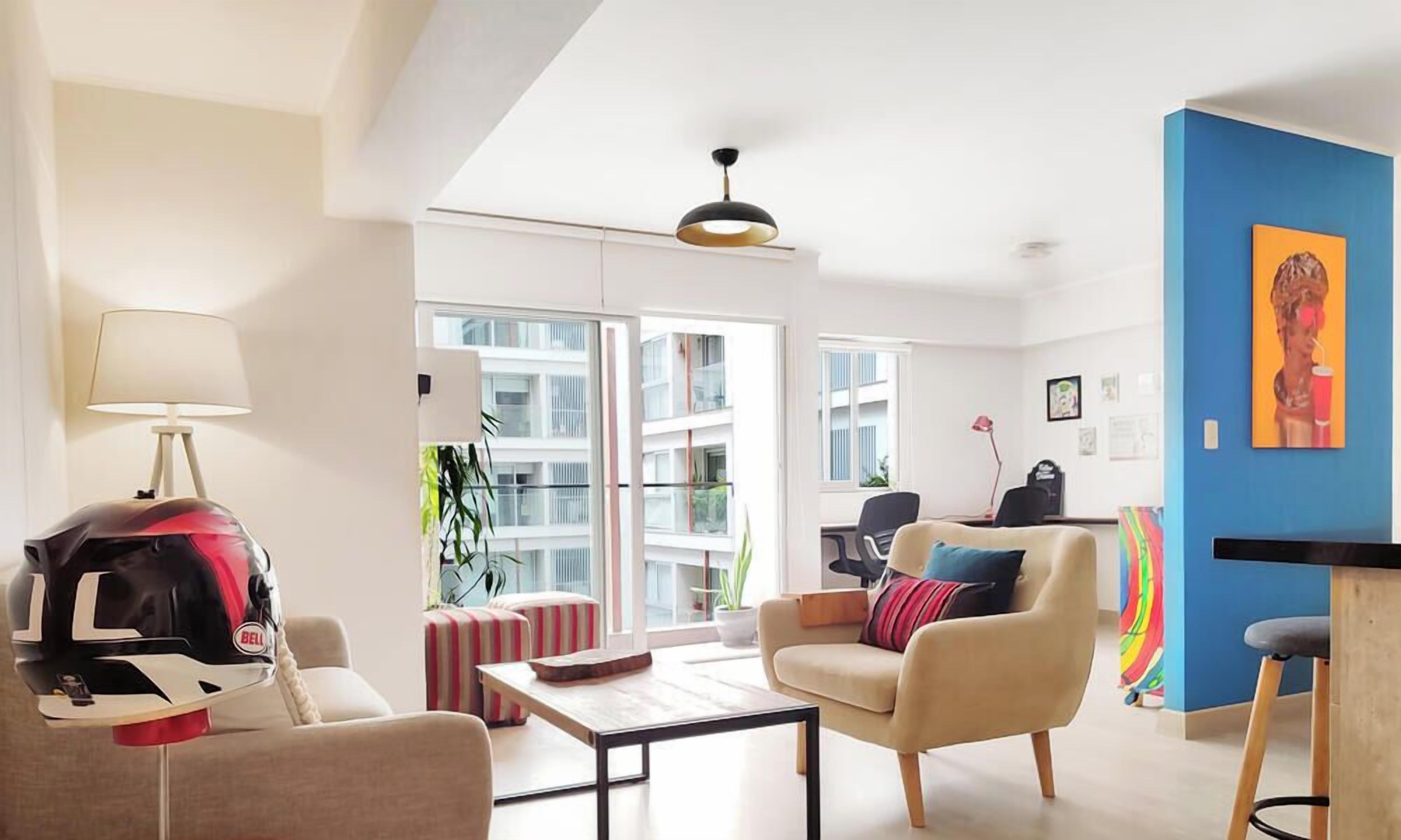 Uma sala de estar moderna com sofá, poltrona, mesa de centro e um capacete no chão.