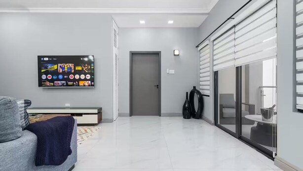 A modern living room with a flat-screen TV mounted on the wall, a grey sofa, a coffee table, and a sliding glass door leading to a balcony. - Coastal Escape in Riviera, Tower Isle - Beach Nearby (St Ann )