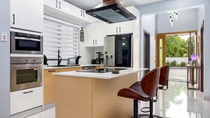 A modern kitchen with a central island, built-in appliances, and a bar stool. - Coastal Escape in Riviera, Tower Isle - Beach Nearby (St Ann )
