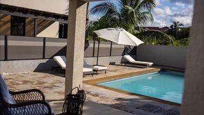 A poolside area with lounge chairs, a table, and a decorative plant. - Coastal Escape in Riviera, Tower Isle - Beach Nearby (St Ann )