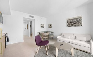 Ein modernes Wohnzimmer mit einer Couch, einem violetten Sessel, einem runden Couchtisch und einem kleinen Esstisch mit Stühlen.