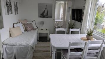 Habitación pequeña con cama, una mesa de comedor y sillas. Cuenta con ventana con cortinas, lámpara y obras de arte en las paredes.