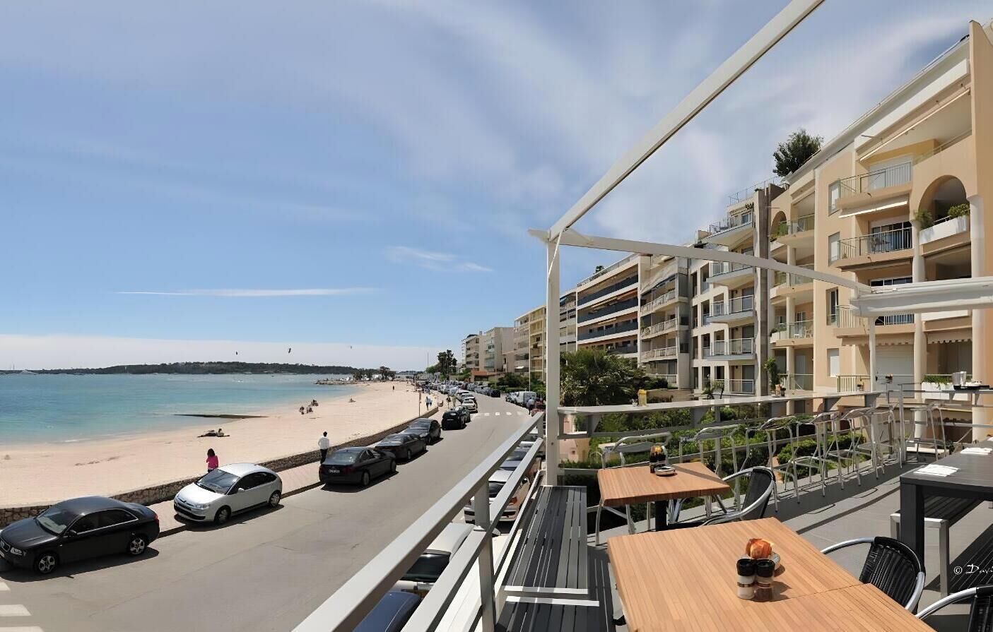A beachfront hotel with multiple balconies, a beach view, and a street with parked cars.