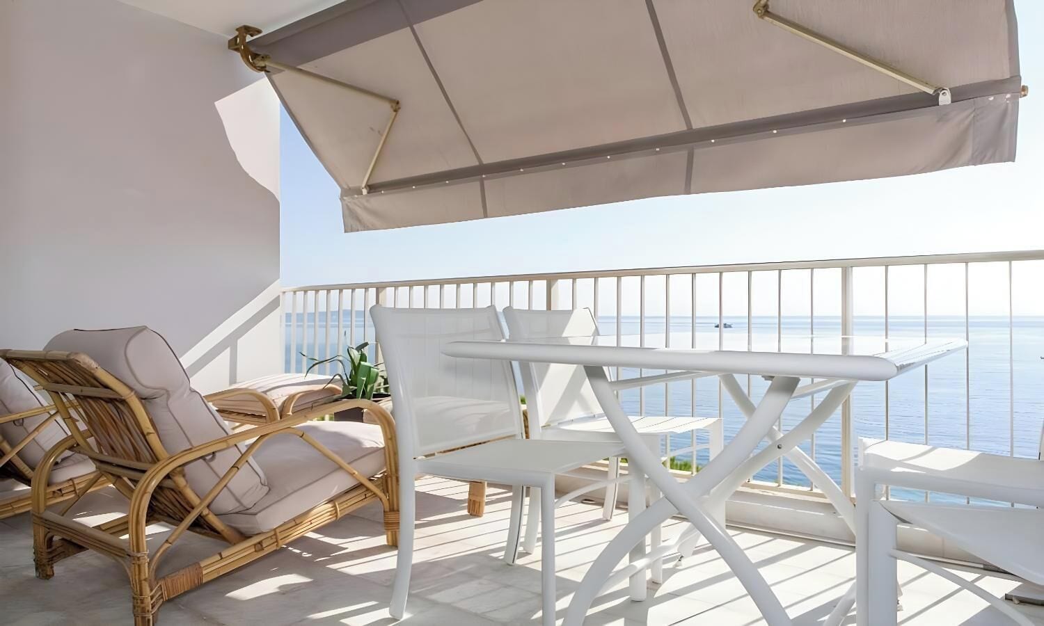A balcony with wicker furniture and a white table, overlooking the sea.