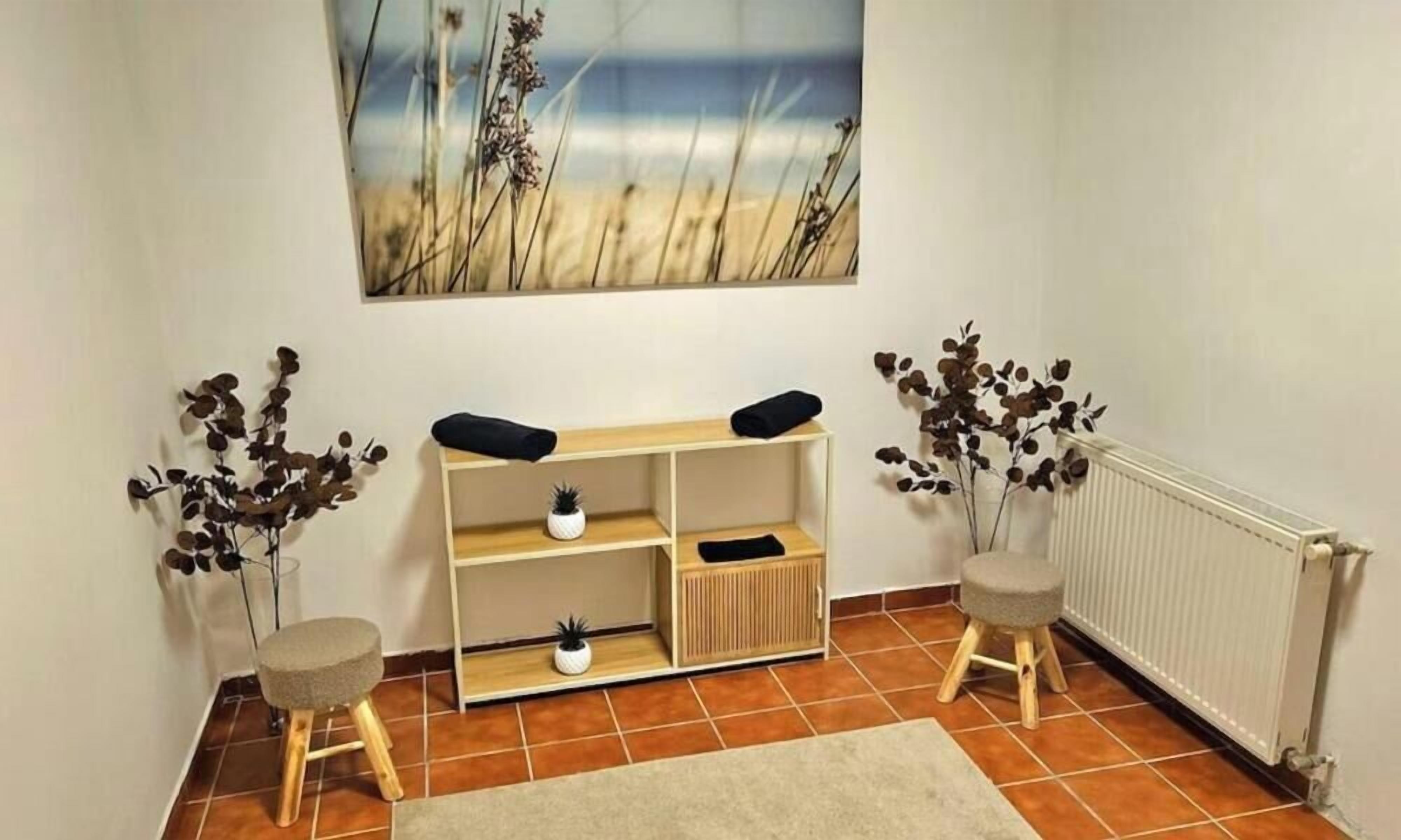 Una habitación con una consola de madera, dos taburetes pequeños, un radiador y un cuadro de una playa.