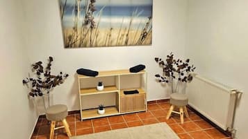 Una habitación con una consola de madera, dos taburetes pequeños, un radiador y un cuadro de una playa.