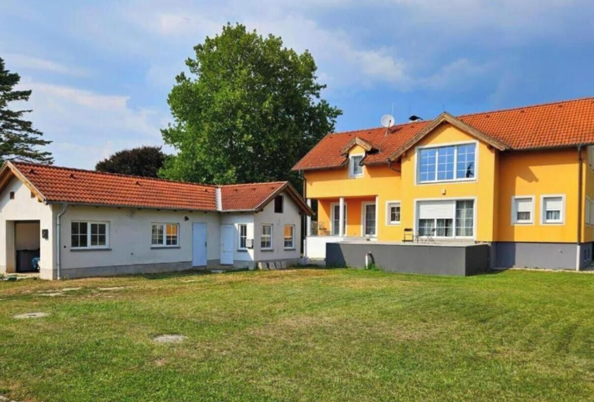 Een rij tweelaagse huizen met rode dakpannen, een gazon en een grote boom op de achtergrond.