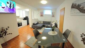 Een moderne woonkamer met een eettafel, bank en keuken op de achtergrond.