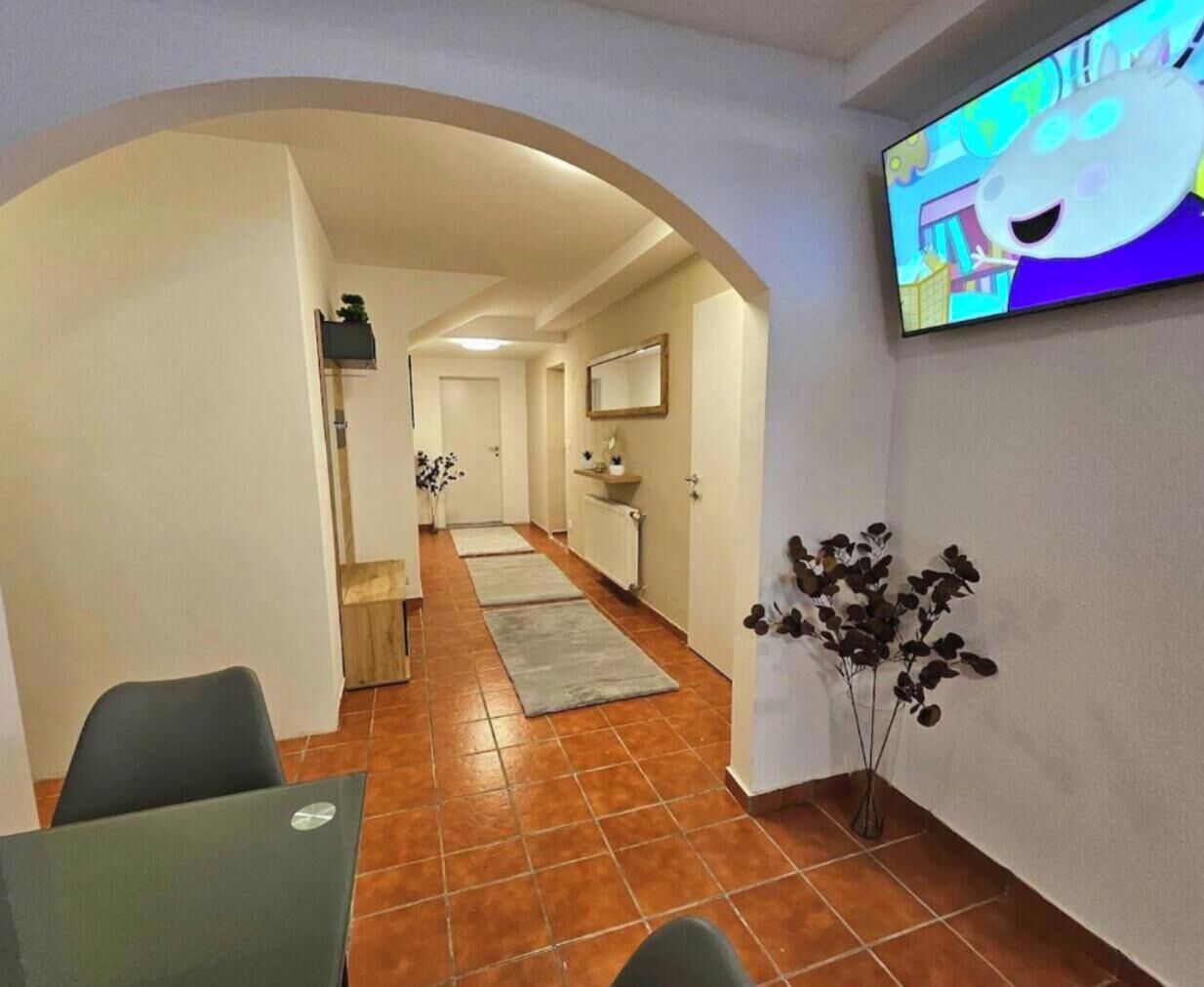 Un pasillo con comedor, televisor montado en la pared y una planta.