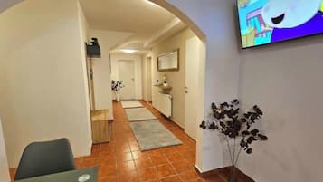 Un pasillo con comedor, televisor montado en la pared y una planta.