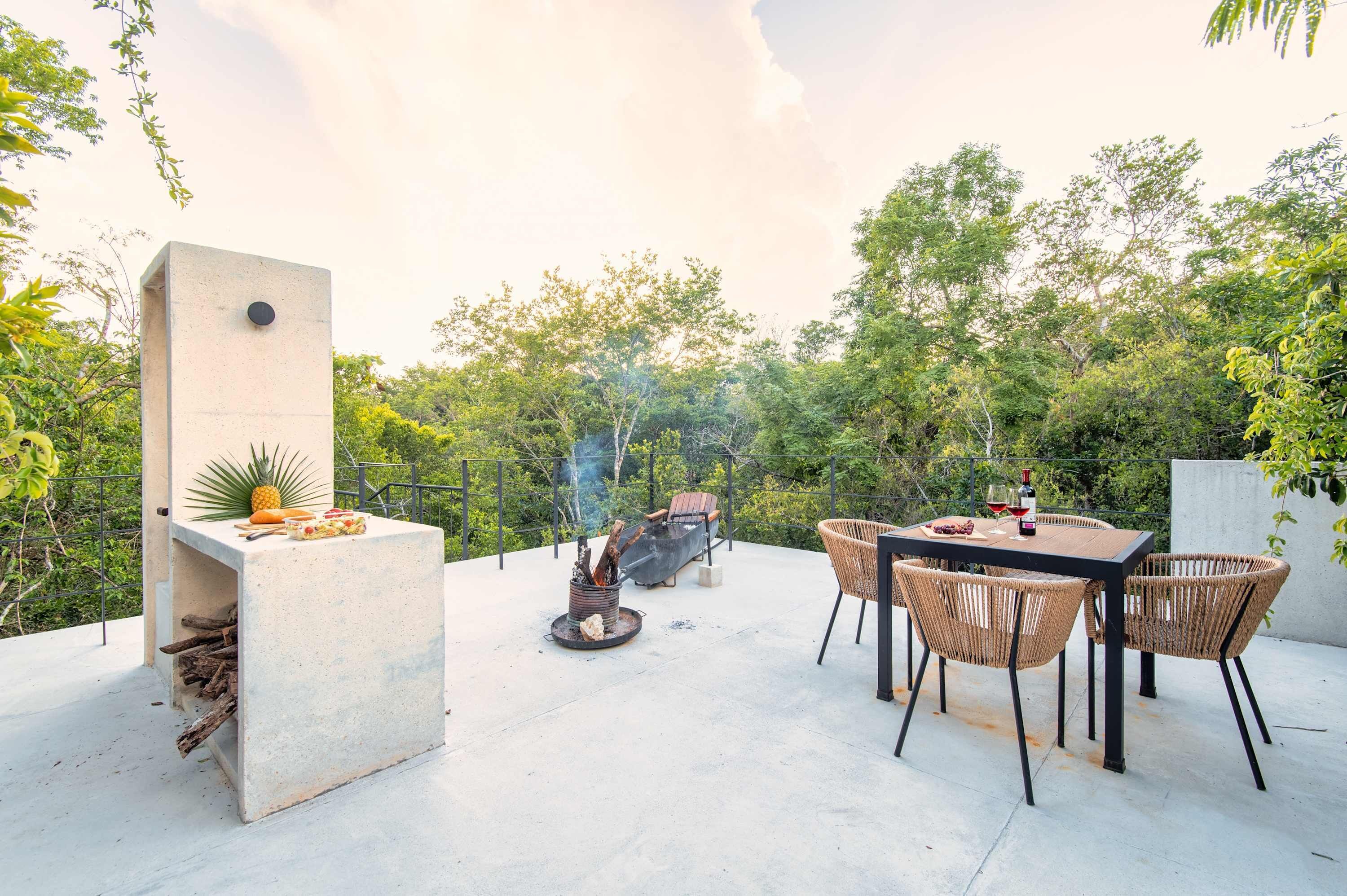 An outdoor patio with a concrete table, wicker chairs, a barbecue grill, and a fire pit.