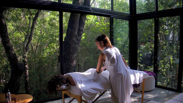 A room with a massage table, a person attending to a client, and a view of a forest through large windows. - Tree60:· Jungle Villa Private Rooftop&Wood-Hot Tub (Chemuyil)