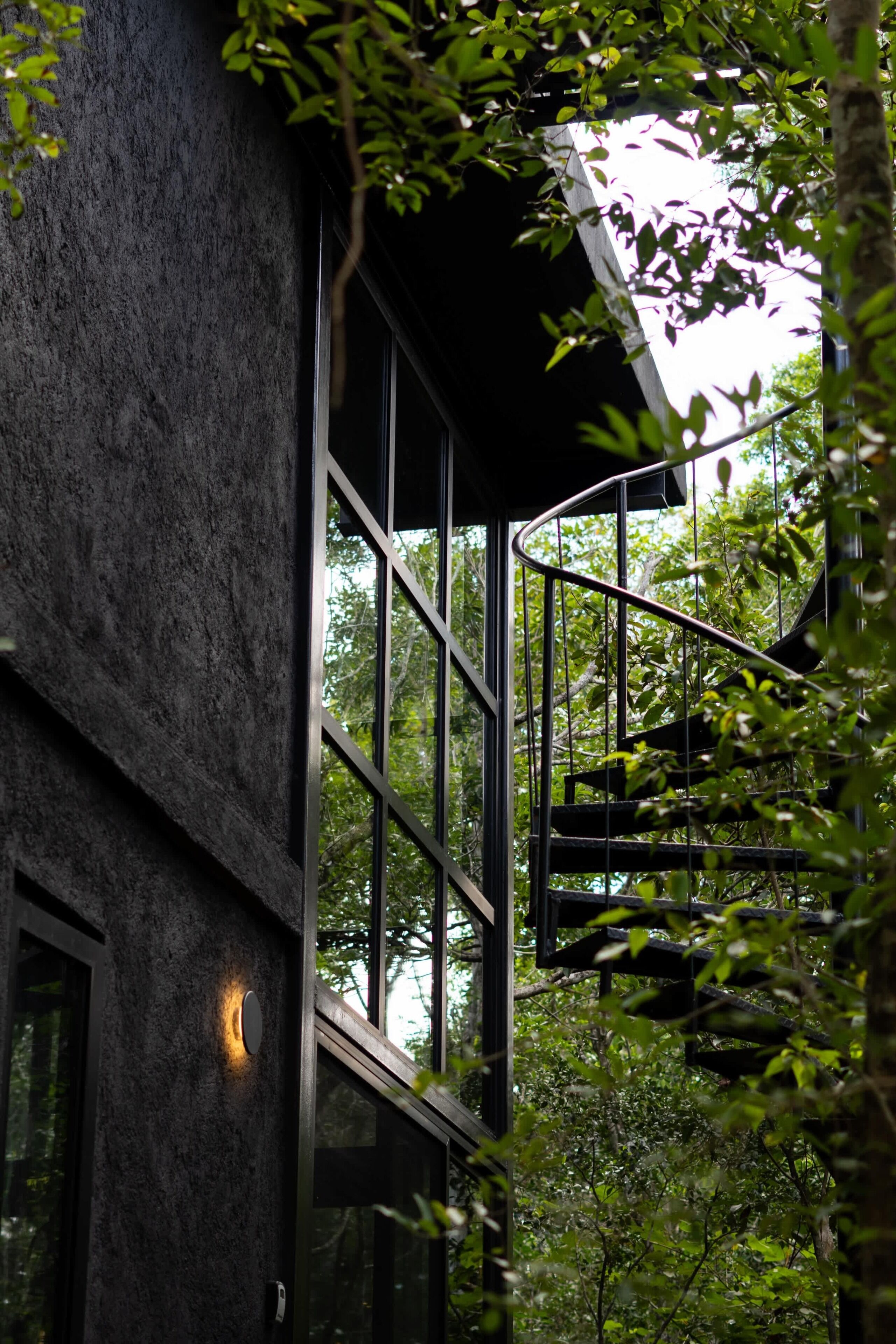 Un edificio moderno con una escalera de caracol, ventanas grandes y una pared texturizada.