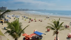 Uma praia com guarda-sóis e cadeiras de praia, palmeiras e céu claro.