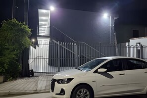 A white car parked in front of a gated entrance with a staircase leading to a building.